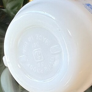 以下が含まれることがあります： 丸みを帯びた底の白いセラミックマグ。マグの底には「MADE IN USA」と「OVENPROOF 36」のエンボス加工された文字があります。マグは滑らかで光沢のある仕上がりです。