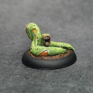 Puede incluir: Una criatura de fantasía en miniatura pintada a mano con un cuerpo verde texturizado y una boca abierta. La figura descansa sobre una base marrón con un borde negro, sobre un fondo gris. Ideal para juegos de mesa.