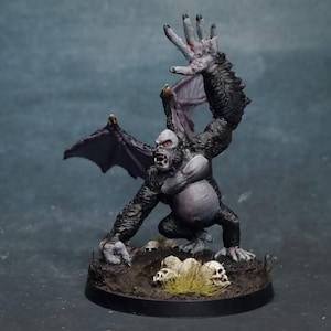 Puede incluir: Una figura en miniatura de una criatura monstruosa, una figura parecida a un gorila con alas de murciélago y un brazo levantado. La figura está pintada en tonos de gris, negro y morado, con ojos rojos y una expresión amenazante. Pequeñas calaveras y hierba en la base.