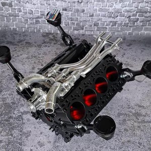 Op de afbeelding: Een salontafel gemaakt van een zwart motorblok met vier uitstekende zuigerpoten, een zilverkleurig inlaatspruitstuk en vier cilindervormige openingen verlicht met dieprood licht. Een kleine afstandsbediening rust op een van de zuigers.