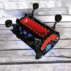 Könnte beinhalten: Ein schwarzer und roter Motorblock-Couchtisch mit Chrom-Akzenten und blauen LED-Lichtern. Der Tisch ist so gestaltet, dass er wie ein echter Motorblock aussieht und eine Glasplatte hat.