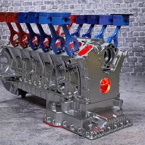 May include: A metallic silver engine block featuring a series of upright pistons and connecting rods in alternating red and blue colors. The engine assembly displays a complex mechanical structure with a bright red circular light accent on the front.