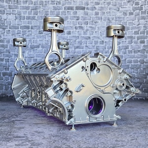 Könnte beinhalten: Ein silberner Motorblock mit vier daran befestigten silbernen Kolben. Der Motorblock wird als Tisch verwendet, wobei ein violettes Licht durch die Mitte des Blocks scheint.