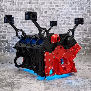 Könnte beinhalten: Ein roter und schwarzer Motorblock-Couchtisch mit vier schwarzen Metallarmen, die sich von oben erstrecken. Der Tisch ist von unten mit blauen LED-Lichtern beleuchtet.