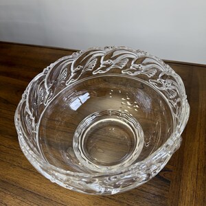 May include: Clear glass serving bowl with a decorative dolphin design around the rim. The bowl has a smaller, circular bowl in the center. The bowl is sitting on a wooden surface.