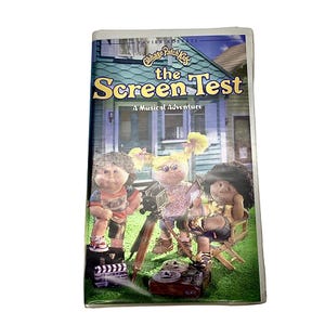 May include: A VHS tape featuring the Cabbage Patch Kids in a musical adventure called "The Screen Test". The cover shows three Cabbage Patch Kids dressed in colourful outfits, holding a movie camera and a script.