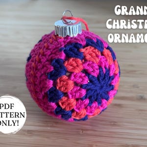 May include: A colourful, crocheted Christmas bauble featuring a granny square pattern in shades of pink, orange, and blue. It has a silver metal cap and a red hanging loop. The image includes text that reads "Granny Christmas Ornament" and "PDF Pattern Only!"