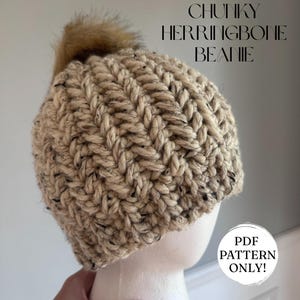 May include: Chunky herringbone beanie in beige and black, with a faux fur pom-pom. The hat is displayed on a mannequin head. Text on the image reads "CHUNKY HERRINGBONE BEANIE" and "PDF PATTERN ONLY!"