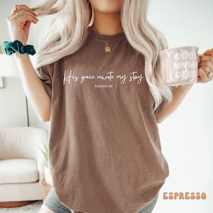May include: A brown t-shirt with the text 'His grace rewrote my story' and 'EPHESIANS 2:10' in white text.
