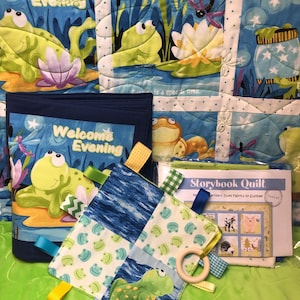 May include: A baby quilt and matching accessories featuring a frog theme. The quilt has frog illustrations and the words "Welcome Evening." A tag blanket with a wooden ring and colorful ribbons is also present. A "Storybook Quilt" pattern is included.