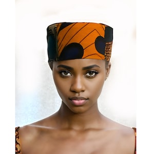 Może przedstawiać: Kobieta nosząca żywy, wzorzysty turban. Turban ma mieszankę pomarańczowych, granatowych i brązowych geometrycznych wzorów. Kobieta ma ciemną skórę i patrzy prosto w kamerę.