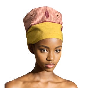 May include: A yellow and pink head wrap with a geometric design. The head wrap has a yellow base with a pink top section featuring a diamond pattern and small perforations. The head wrap is a traditional style.