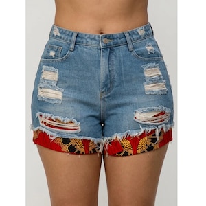 May include: High-waisted blue denim shorts featuring distressed rips and frayed edges. The hem is accented with a vibrant red, yellow, and black patterned fabric trim that extends from underneath the denim, creating a layered appearance.