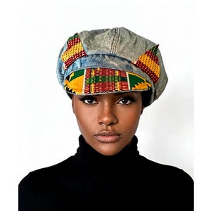 May include: A denim newsboy cap with colorful African print fabric accents. The cap features a brim and is adorned with yellow, green, red, and black patterns. The cap is worn with a black turtleneck.