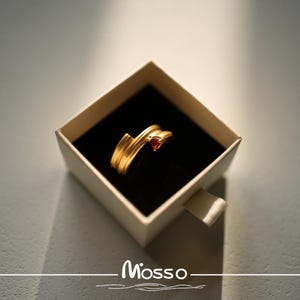 May include: A gold ring with a red gemstone in a white box. The box has the word "Mosso" printed on it.