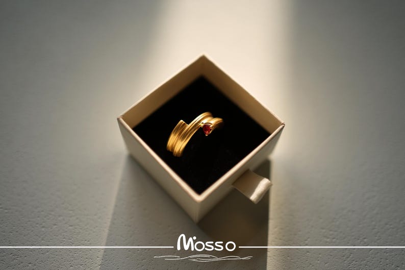 May include: A gold ring with a red gemstone in a white box. The box has the word "Mosso" printed on it.