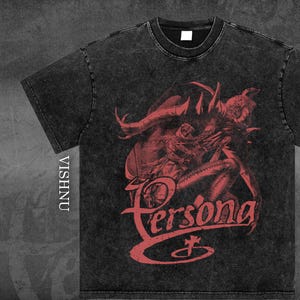 Puede incluir: Camiseta gris oscuro con un gráfico rojo de una figura demoníaca y la palabra "Persona" en una fuente estilizada. La camiseta tiene un aspecto vintage y desgastado, y la marca "VISHNU" está impresa verticalmente en el lado izquierdo.