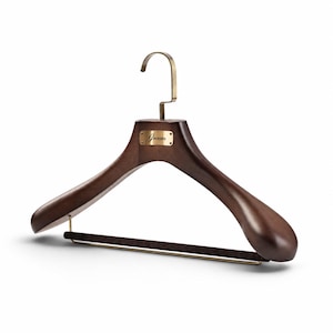 May include: A dark brown wooden clothes hanger with wide, contoured shoulders, a brass-colored metal hook, and a horizontal bar covered in dark brown velvet. A rectangular brass-colored metal plate is attached to the center with the word Groom.