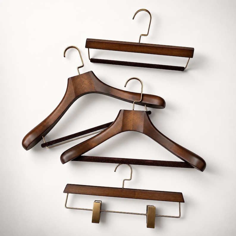 May include: A collection of four dark brown wooden clothes hangers with brass-toned metal hooks. Two hangers feature wide, contoured shoulders, one includes a horizontal bar with a dark velvet grip, and one has a bar with two adjustable clips.