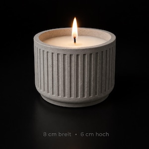 K&ouml;nnte beinhalten: Eine brennende Kerze in einem grauen Betonbeh&auml;lter. Die Kerze hat wei&szlig;es Wachs und eine helle gelbe Flamme. Der Beh&auml;lter ist 8 cm breit und 6 cm hoch und hat vertikale Rippendetails. Der Text unten lautet: 8 cm breit - 6 cm hoch.