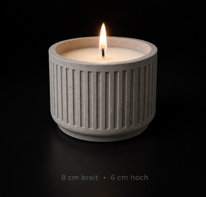 K&ouml;nnte beinhalten: Eine brennende Kerze in einem grauen Betonbeh&auml;lter. Die Kerze hat wei&szlig;es Wachs und eine helle gelbe Flamme. Der Beh&auml;lter ist 8 cm breit und 6 cm hoch und hat vertikale Rippendetails. Der Text unten lautet: 8 cm breit - 6 cm hoch.