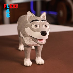 Puede incluir: Una figurita de lobo gris con pecho y patas blancas. El lobo tiene una expresión amigable con la boca ligeramente abierta y ojos negros. La figurita está de pie sobre una superficie marrón.