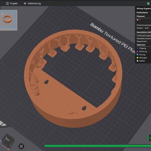 May include: A 3D-printed, orange-brown object with a circular shape and a section cut out. The object has a textured surface and a series of curved, tooth-like structures along the outer edge. Two small holes are visible within the cut-out section.