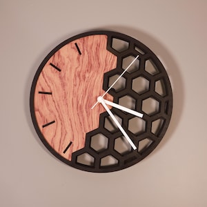 May include: A round wooden clock with a honeycomb design on one half and a wood grain pattern on the other half. The clock has white hands and black numbers.