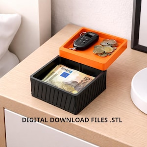 Puede incluir: Una caja de almacenamiento cuadrada negra y naranja con tapa. La tapa naranja contiene un llavero de coche y monedas. La caja contiene billetes. El texto "DIGITAL DOWNLOAD FILES .STL" está en la parte inferior.