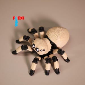 Könnte beinhalten: Eine beige und schwarze Spinnenfigur mit mehreren Augen und segmentierten Beinen. Die Spinne hat einen abgerundeten Hinterleib und ist mit gespreizten Beinen dargestellt. Der Text "FLEXI AB" ist in der oberen linken Ecke sichtbar.
