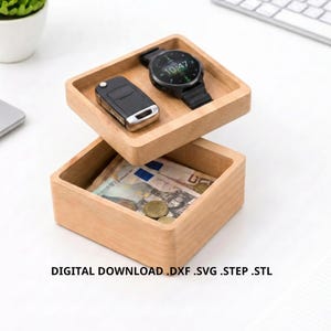 Könnte beinhalten: Zweistöckige Holzaufbewahrungsbox mit quadratischem Design. Das obere Fach enthält einen Autoschlüsselanhänger und eine schwarze Smartwatch. Das untere Fach enthält Papiergeld und Münzen. Der Text "DIGITAL DOWNLOAD .DXF .SVG .STEP .STL" befindet sich unten.