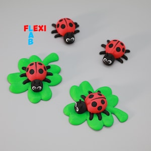 May include: Four ladybug-themed decorations. Two ladybugs are on green four-leaf clovers, and two ladybugs are by themselves. The ladybugs are red with black spots and black heads. The text "FLEXI AB" is in the upper left corner.