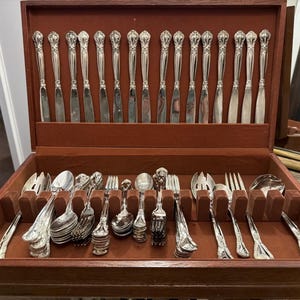 May include: A wooden cutlery chest with a red velvet interior, containing a full set of ornate silver utensils. The set includes knives, forks, spoons, and serving pieces, all with decorative handles.