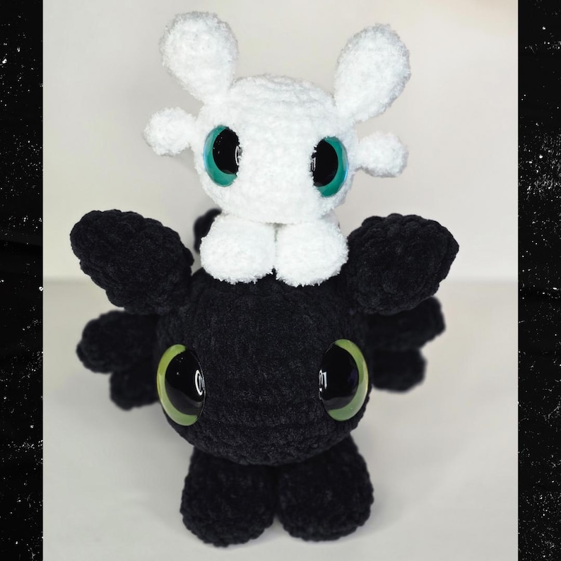 Puede incluir: Un peluche hecho a mano con un drag&oacute;n negro con grandes ojos verdes y una criatura blanca con ojos verdes encaramada encima. Los juguetes est&aacute;n hechos de un material suave y texturizado.