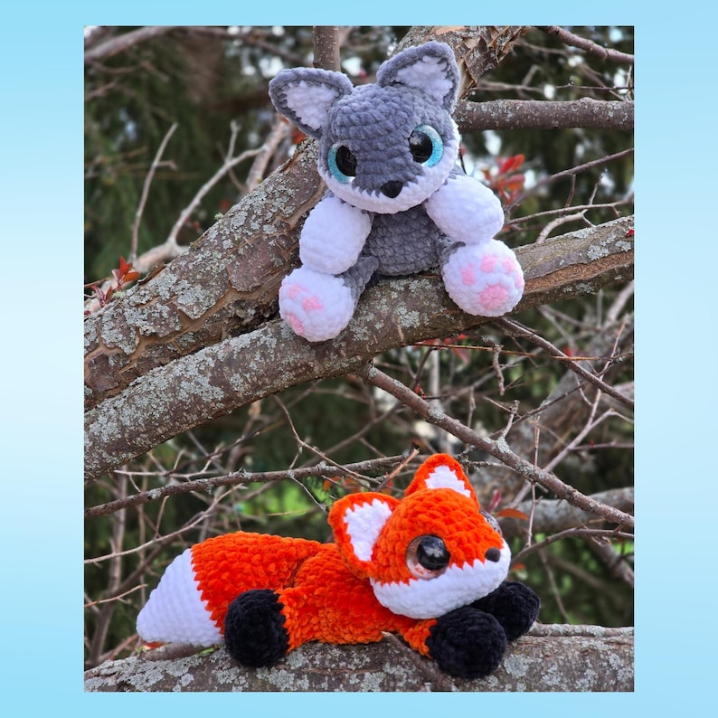 Puede incluir: Dos animales de peluche hechos a mano con ganchillo: un lobo gris con detalles blancos y rosas, y un zorro naranja con detalles blancos y negros. Ambos tienen ojos grandes y expresivos y est&aacute;n posados en una rama.