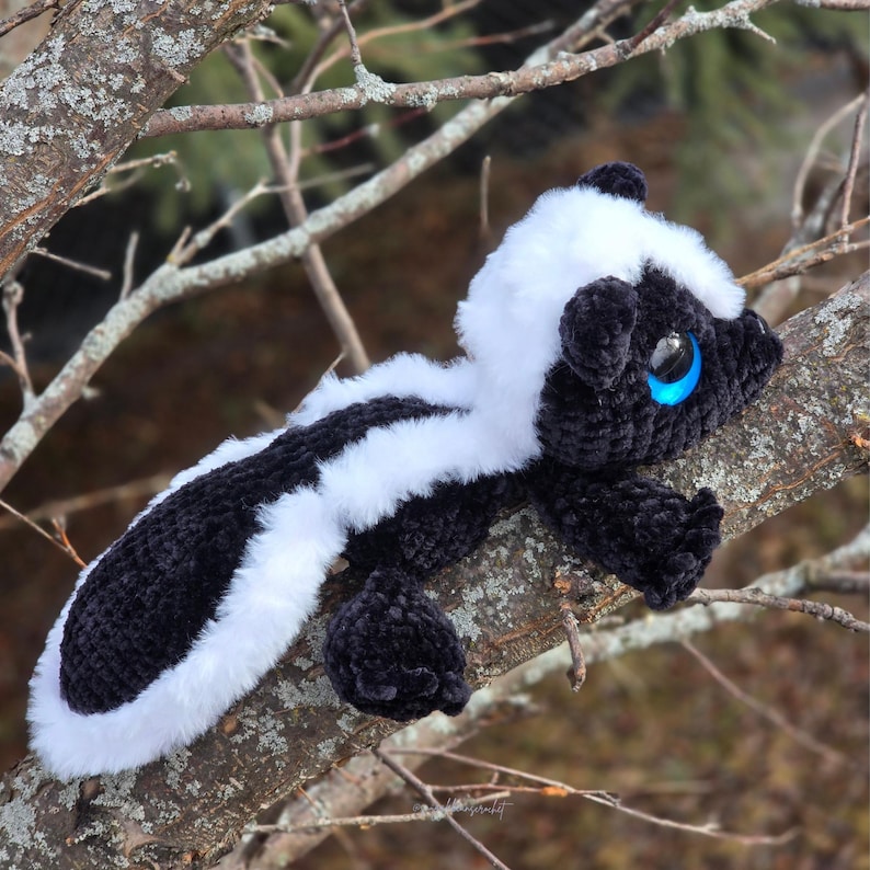 May include: A handcrafted skunk plush toy with a black and white striped design, white fluffy fur, and large blue eyes. The skunk is positioned on a tree branch, highlighting its soft, tactile qualities. This charming soft toy is suitable for children and collectors.