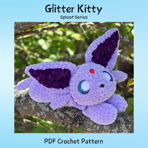 Könnte beinhalten: Ein gehäkeltes Tier in Lavendelfarbe mit großen Ohren und einem roten Punkt auf der Stirn. Der Text "Glitter Kitty Sploot Series" steht oben und "PDF Crochet Pattern" unten. Das Tier liegt auf einem Ast.