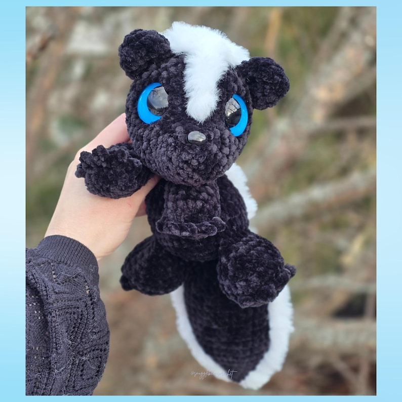 May include: A handmade crochet skunk plush toy. The skunk is black with a white stripe down its back and a white tail. It has large blue eyes and a white stripe on its head. A soft, cuddly toy, suitable for a child's room or as a decorative item.