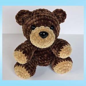 May include: A handmade brown teddy bear with a tan muzzle, paws, and inner ears. The bear has black button eyes and a black nose. The plush toy is made of a soft, textured material, and is sitting upright.
