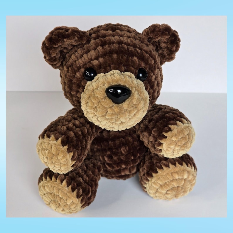 May include: A handmade brown teddy bear with a tan muzzle, paws, and inner ears. The bear has black button eyes and a black nose. The plush toy is made of a soft, textured material, and is sitting upright.