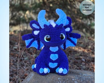 Könnte beinhalten: Ein handgefertigtes blaues Häkeldrachen-Spielzeug mit großen, ausdrucksstarken Augen. Der Drache hat hellblaue Akzente auf seinen Hörnern, Flügeln und Bauch. Der Text "Zazzie The Baby Dragon" und "PDF Crochet Pattern" werden angezeigt.