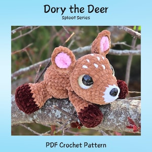 May include: A crocheted deer toy in shades of brown with white spots, pink inner ears, and dark brown hooves. The deer has large, reflective eyes and a white muzzle. The text at the top reads "Dory the Deer" and "Sploot Series."
