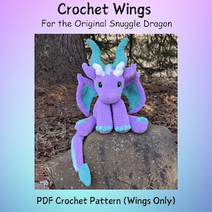 以下が含まれることがあります： ターコイズの翼、角、アクセントが付いた、かぎ針編みの紫色のドラゴンが岩の上に座っています。ドラゴンは大きな黒い目を持ち、長い尻尾があります。上部のテキストは「Crochet Wings For the Original Snuggle Dragon」と書かれています。下部のテキストは「PDF Crochet Pattern（Wings Only）」と書かれています。