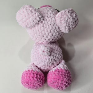 Puede incluir: Un juguete de cerdo de peluche hecho a mano en tonos de rosa. El cerdo tiene orejas grandes y redondeadas, una peque&ntilde;a cola y pies de dos tonos. El juguete est&aacute; hecho de un hilo suave y texturizado, lo que le da una apariencia tierna. La cabeza del cerdo est&aacute; ligeramente inclinada.