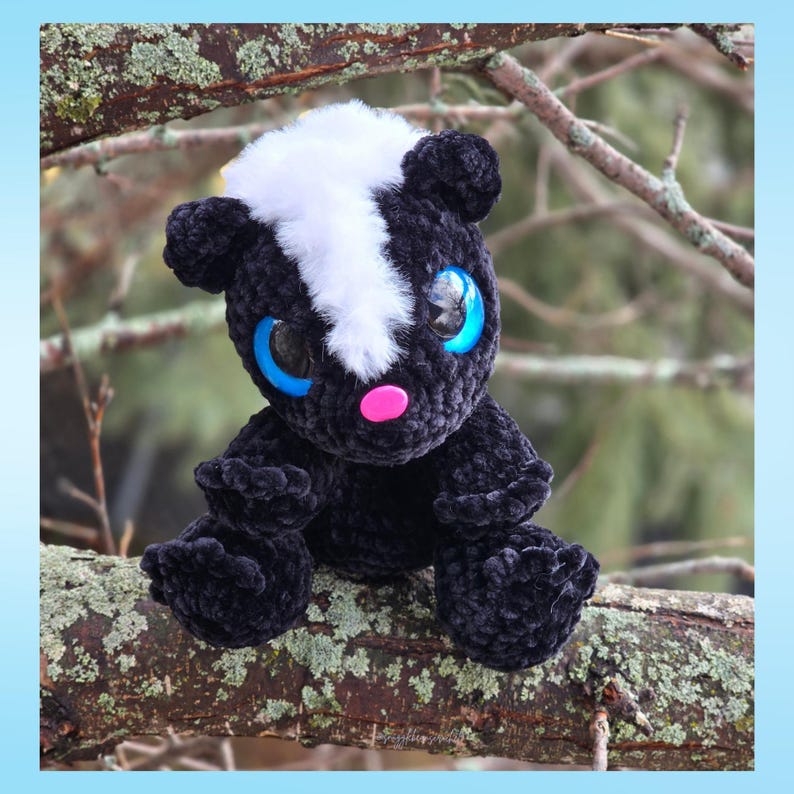 May include: A handmade plush skunk with black, white, and pink details. The skunk has large blue eyes and is sitting on a tree branch. The plush toy is made of soft, textured material.