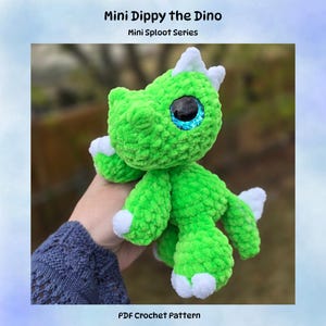 May include: A handmade green crochet dinosaur toy with white accents on its claws and horns. The dinosaur has large, sparkly blue eyes. The text "Mini Dippy the Dino" and "Mini Sploot Series" are at the top, and "PDF Crochet Pattern" is at the bottom.