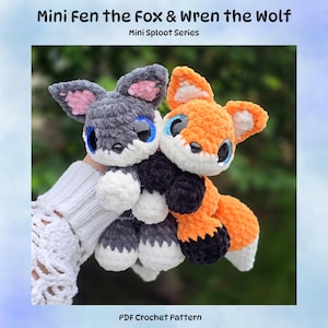 May include: Two plush crochet toys titled Mini Fen the Fox and Wren the Wolf from the Mini Sploot Series. One toy is orange and white with black paws, the other is grey and white with pink inner ears. Both have large blue eyes and black noses.