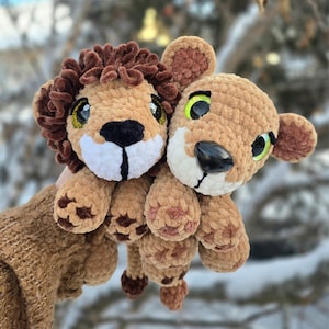 Pode incluir: Dois brinquedos de pel&uacute;cia de le&atilde;o. Um tem uma juba marrom, um nariz preto e um focinho branco. O outro tem um corpo marrom, um nariz preto e olhos verdes. Ambos t&ecirc;m olhos grandes e expressivos e s&atilde;o feitos de um material macio e texturizado.