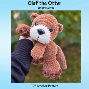 Könnte beinhalten: Ein braun-weißes gehäkeltes Otter-Stofftier mit großen dunklen Augen und einer schwarzen Nase. Der Text Olaf the Otter Sploot Series und PDF Crochet Pattern ist oben und unten im Bild zu sehen und beschreibt den Artikel als Häkelanleitung.