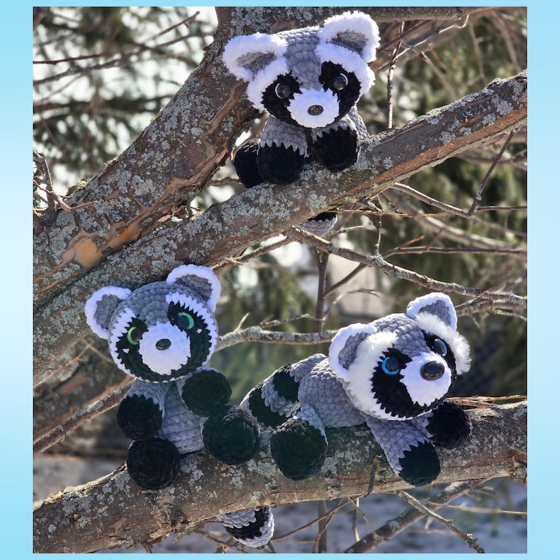 May include: Three crocheted raccoon stuffed animals in gray, white, and black, perched on tree branches. The raccoons have black masks, white ears, and black paws. One raccoon sits, and two are lying down.